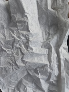 A crumpled and textured white surface resembling tissue paper with various folds and creases creating an abstract pattern.