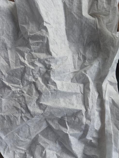 A crumpled and textured white surface resembling tissue paper with various folds and creases creating an abstract pattern.
