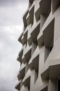 The image features an abstract architectural design with repeating geometric patterns on the facade of a building. The structure consists of protruding rectangular and trapezoidal elements casting distinct shadows, creating a three-dimensional effect.