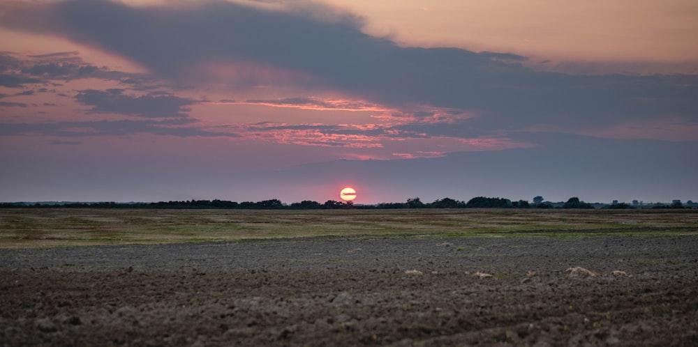 the sun is setting over the horizon of a field