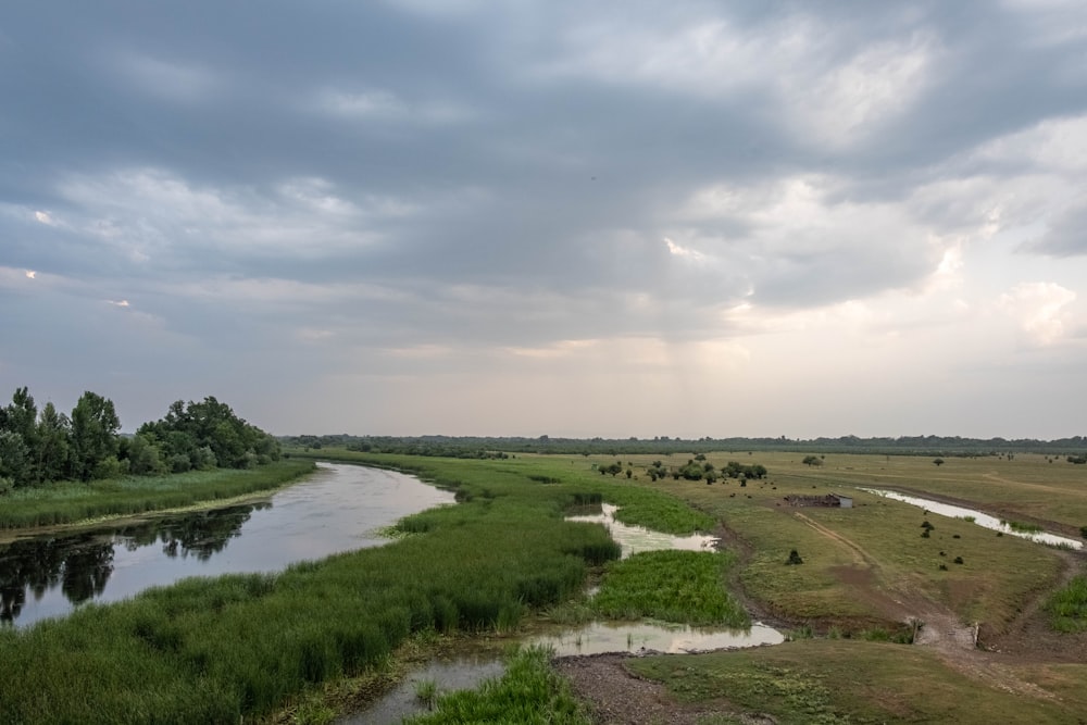 a river running through a lush green field under a cloudy sky