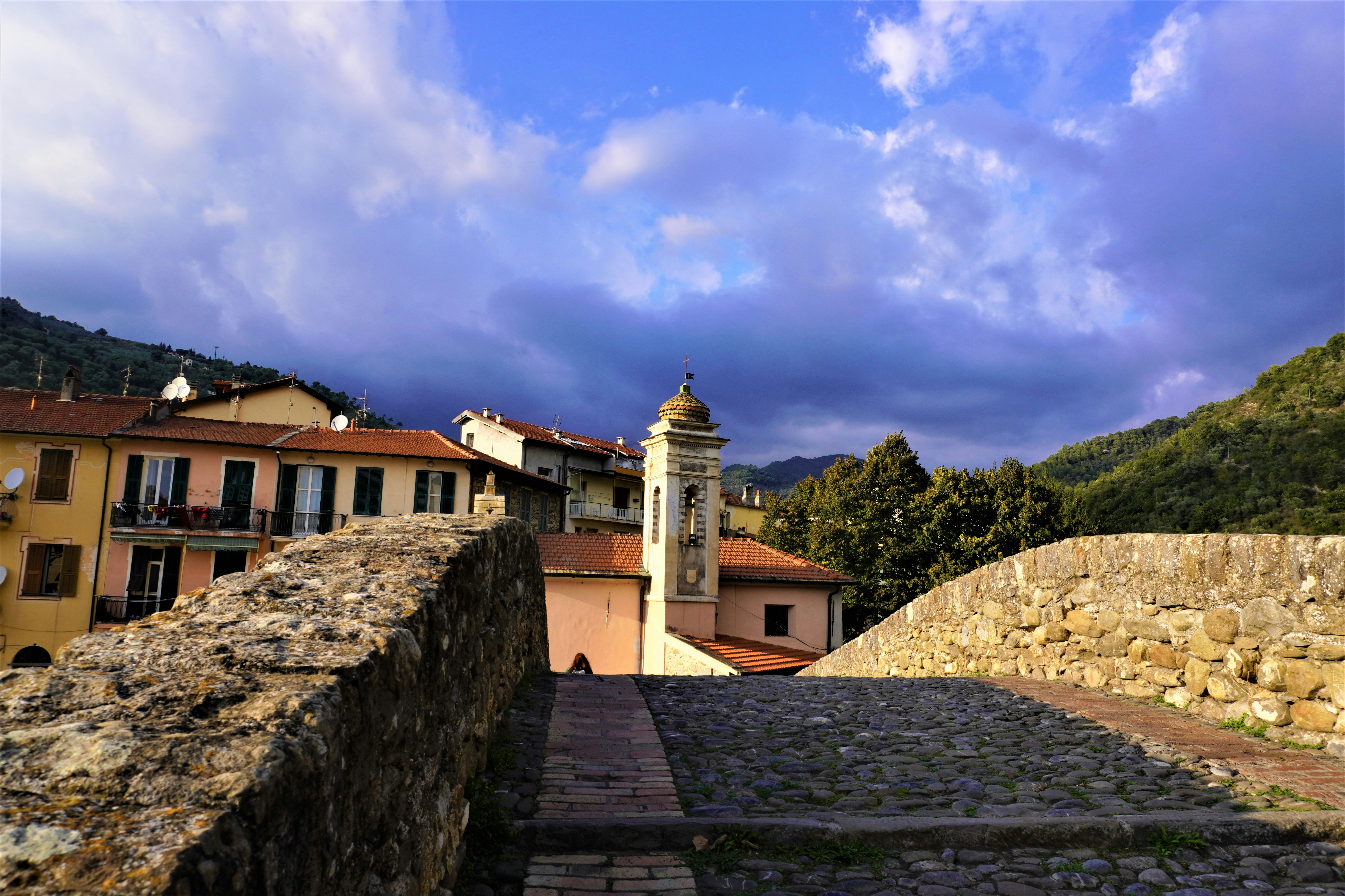 a stone wall with a clock tower in the background, church, architecture, building, religion, tower, stone, sky, ancient, old, europe, monastery, spain, travel, landmark, chapel, cathedral, monument, temple, cross, town, medieval, mountain, history, house, wall