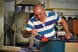 a man in a blue and white striped shirt working on a piece of metal