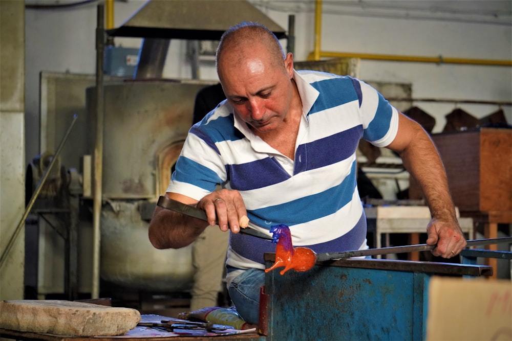 a man in a blue and white striped shirt working on a piece of metal