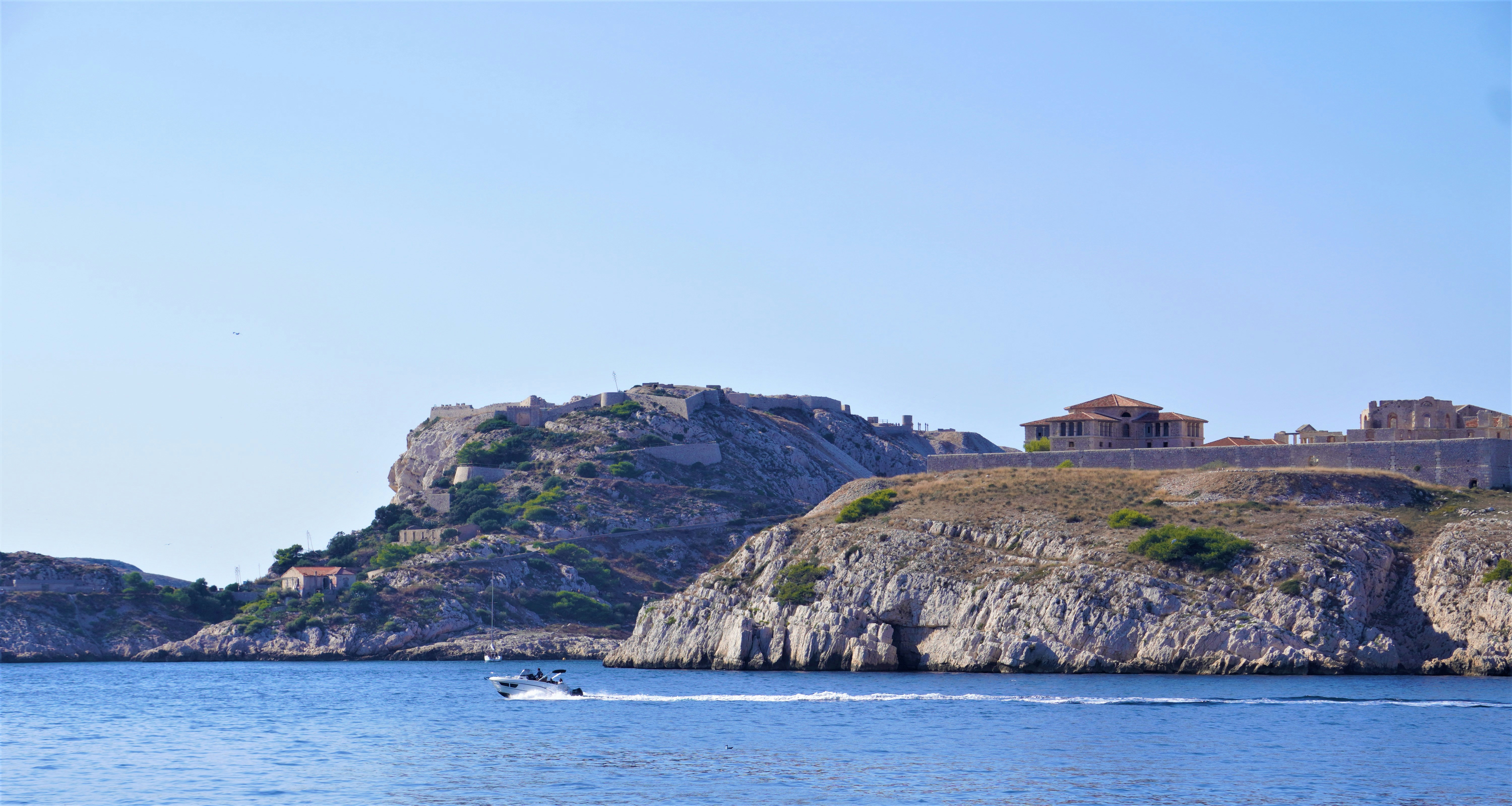 a boat is in the water near a castle, sea, water, island, coast, landscape, travel, nature, summer, sky, beach, mediterranean, bay, rock, ocean, tourism, greece, italy, view, croatia, boat, europe, spain, port, holiday, mountains