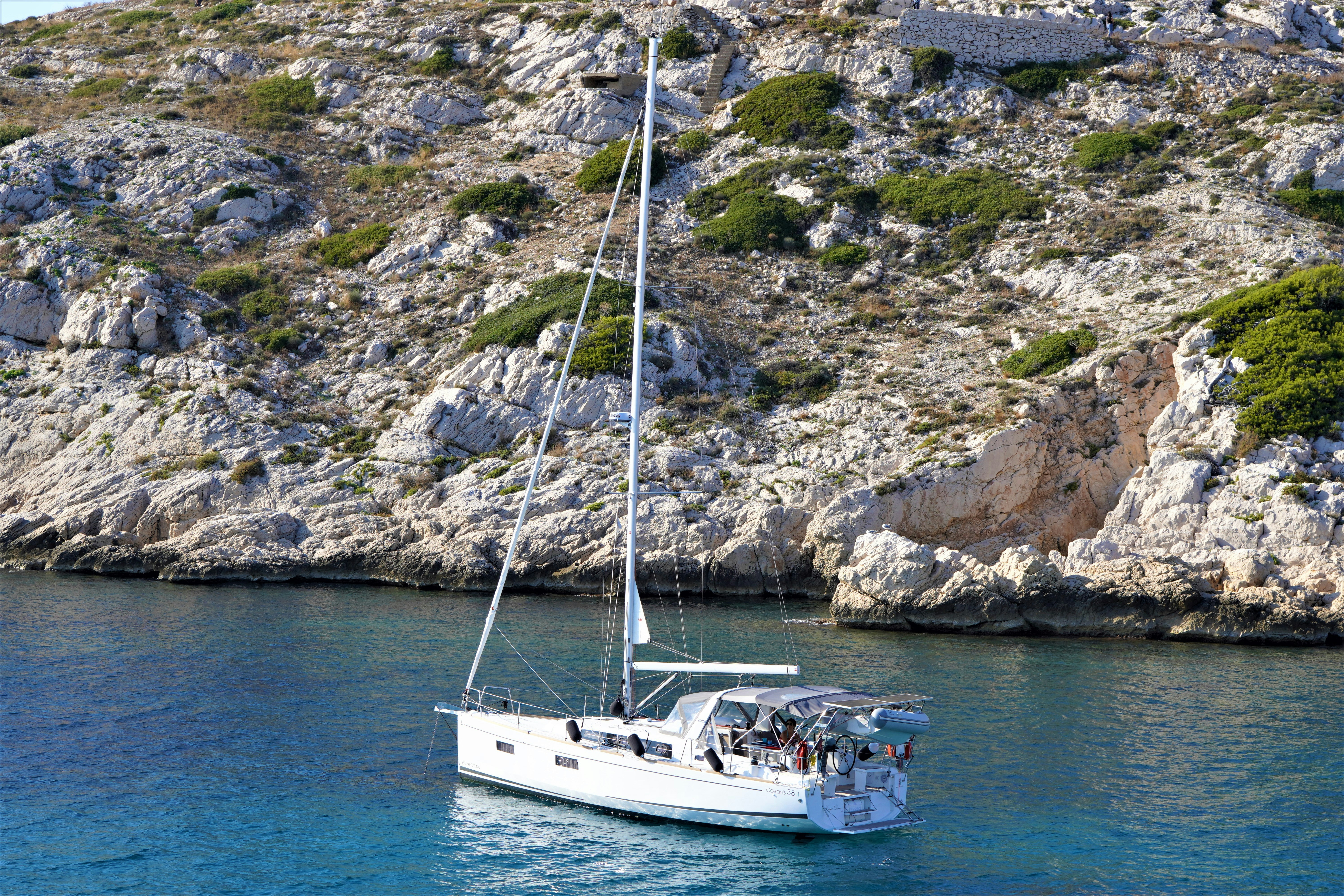a sailboat in the water near a rocky shore, sea, boat, yacht, water, sailing, ship, sailboat, sail, sky, travel, summer, bay, ocean, mediterranean, boats, vacation, coast, island, holiday, tourism, cruise, landscape, beach, catamaran, harbor