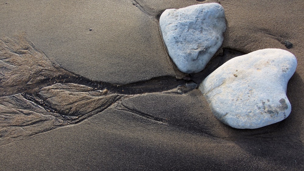 a couple of rocks sitting on top of a sandy beach