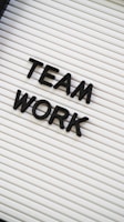 Black plastic letters forming the words 'TEAM WORK' are placed on a white letter board with horizontal grooves.