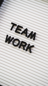 Black plastic letters forming the words 'TEAM WORK' are placed on a white letter board with horizontal grooves.