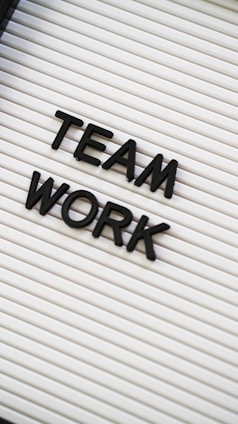 Black plastic letters forming the words 'TEAM WORK' are placed on a white letter board with horizontal grooves.