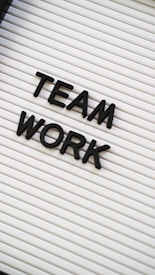 Black plastic letters forming the words 'TEAM WORK' are placed on a white letter board with horizontal grooves.