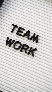 Black plastic letters forming the words 'TEAM WORK' are placed on a white letter board with horizontal grooves.