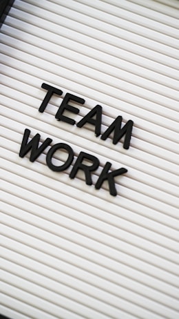 Black plastic letters forming the words 'TEAM WORK' are placed on a white letter board with horizontal grooves.