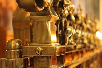 A close-up view of ornate, polished golden metalwork featuring intricate decorative elements. The focus is sharp on the foreground and blurs towards the background, highlighting the detailed craftsmanship.