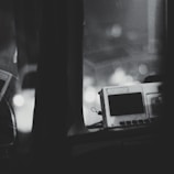 A monochromatic image captures a retro electronic device with a rectangular screen and buttons. It's set on a dark surface with blurred circular lights in the background, creating a bokeh effect. The overall composition feels abstract and minimalistic.