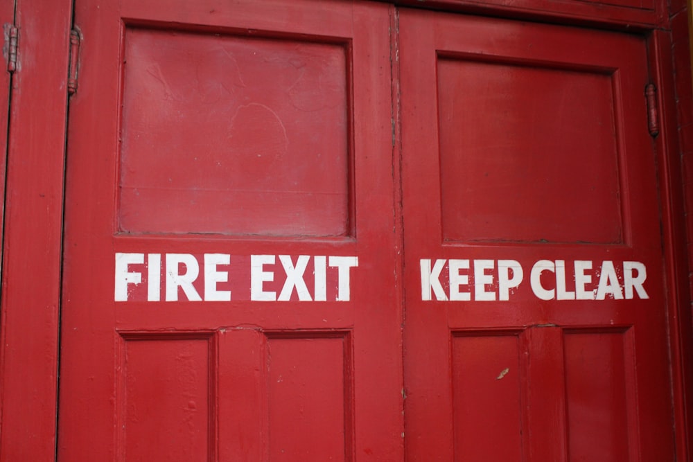 una puerta roja con dos señales de salida de incendios