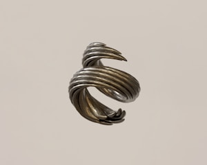 A metallic sculpture with a spiral, twisted design rotates in mid-air. The surface has a silvery, reflective finish with a slightly rough texture.