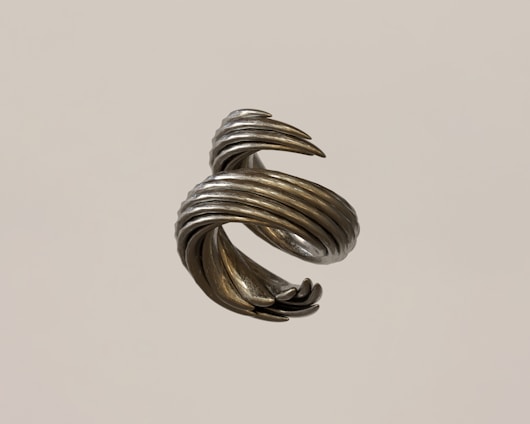 A metallic sculpture with a spiral, twisted design rotates in mid-air. The surface has a silvery, reflective finish with a slightly rough texture.