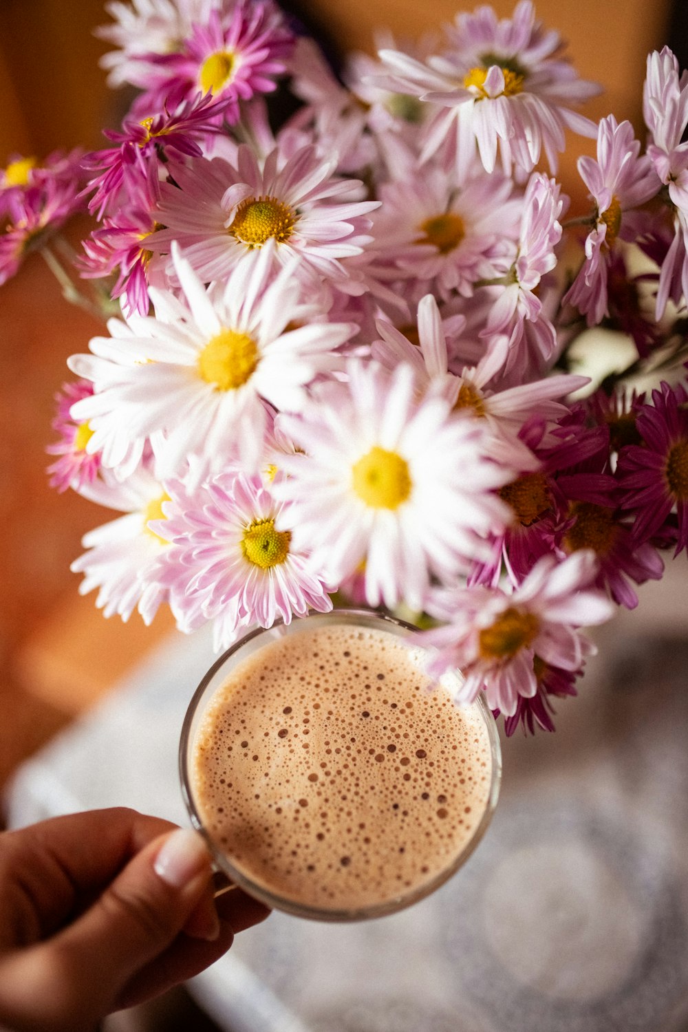 une personne tenant une tasse de café devant un bouquet de fleurs