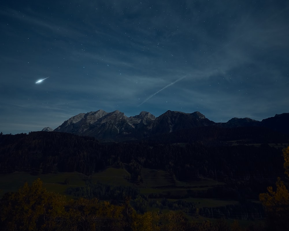 a night sky with the moon and stars above a mountain range