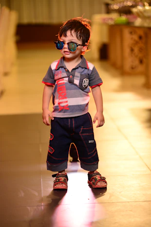 a young boy wearing sunglasses and standing on a tile floor
