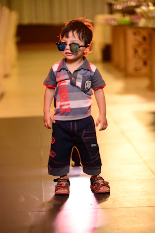 a young boy wearing sunglasses and standing on a tile floor