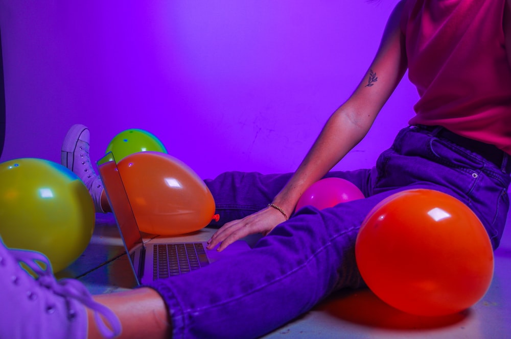 a woman sitting on a laptop with balloons around her