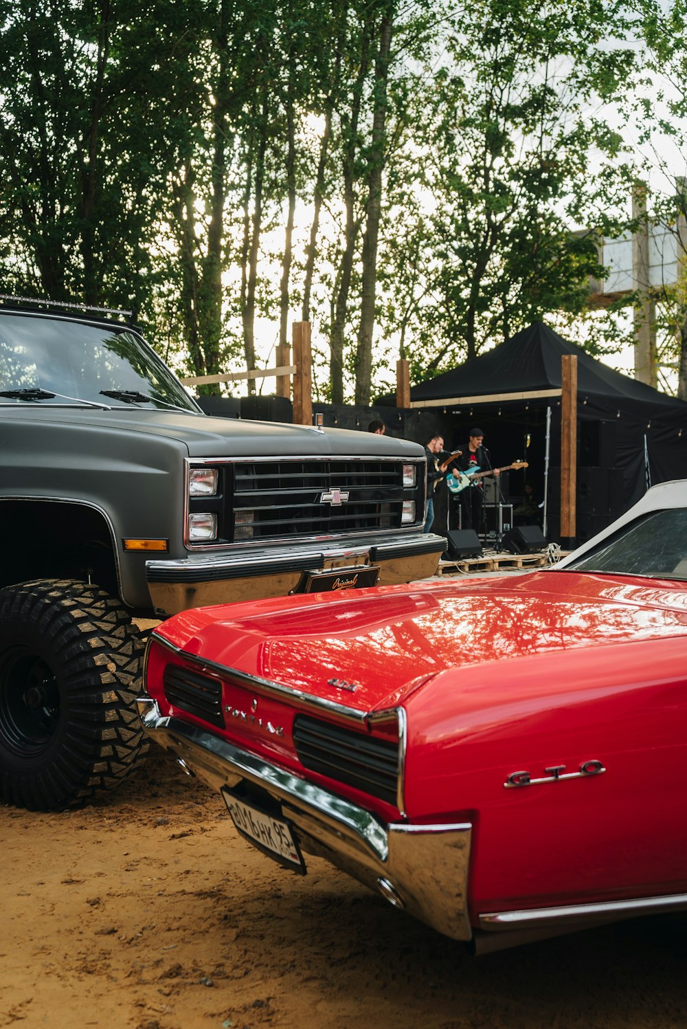 a red car parked next to a truck on a dirt road