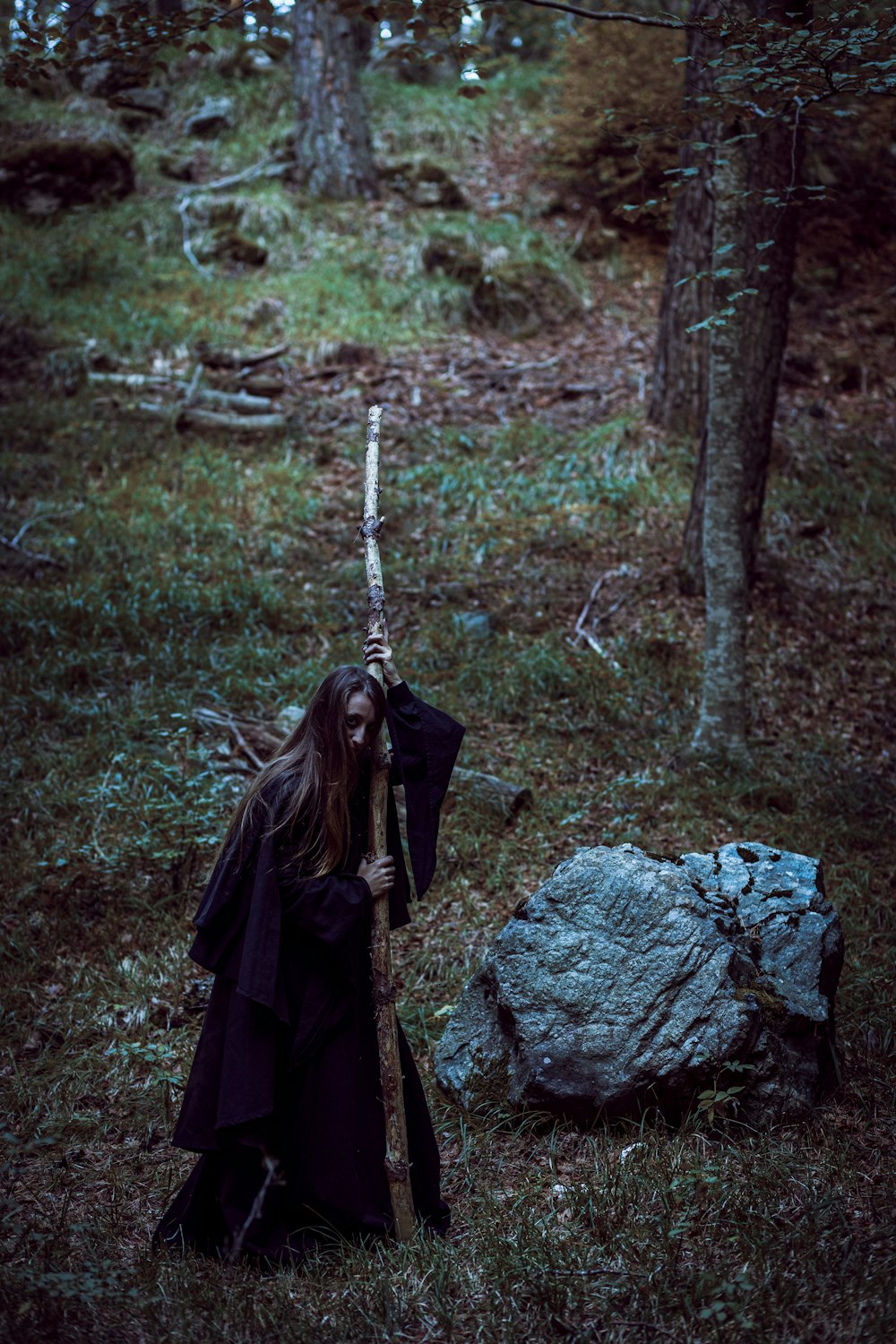 a woman dressed in black holding a stick in a forest