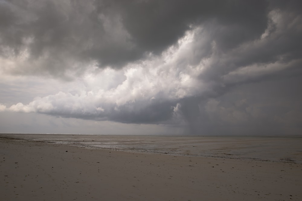 a cloudy sky over a beach with footprints in the sand