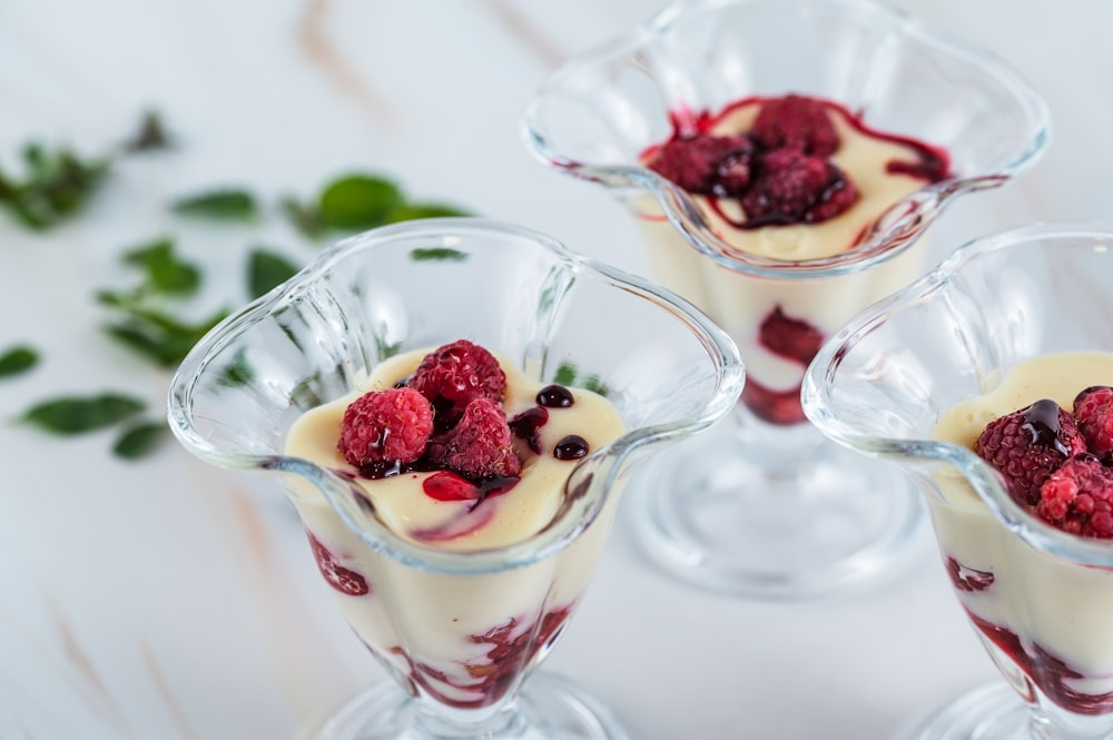 three desserts with raspberries and cream on a table