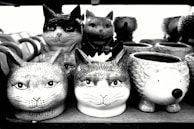 Several ceramic mugs and containers are shaped and painted to look like various animal heads. The majority resemble cats, while one appears to be a hedgehog.