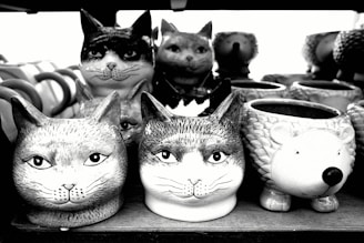 Several ceramic mugs and containers are shaped and painted to look like various animal heads. The majority resemble cats, while one appears to be a hedgehog.