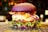 A gourmet burger with a vibrant purple bun, melted cheese, crispy bacon, slices of red onion, tomato, and fresh green lettuce. The burger is placed on a patterned surface with a blurred background featuring warm, ambient lighting.