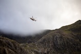 A rugged helicopter lifting off from a makeshift base nestled among twisted trees and orange-tinted ruins.