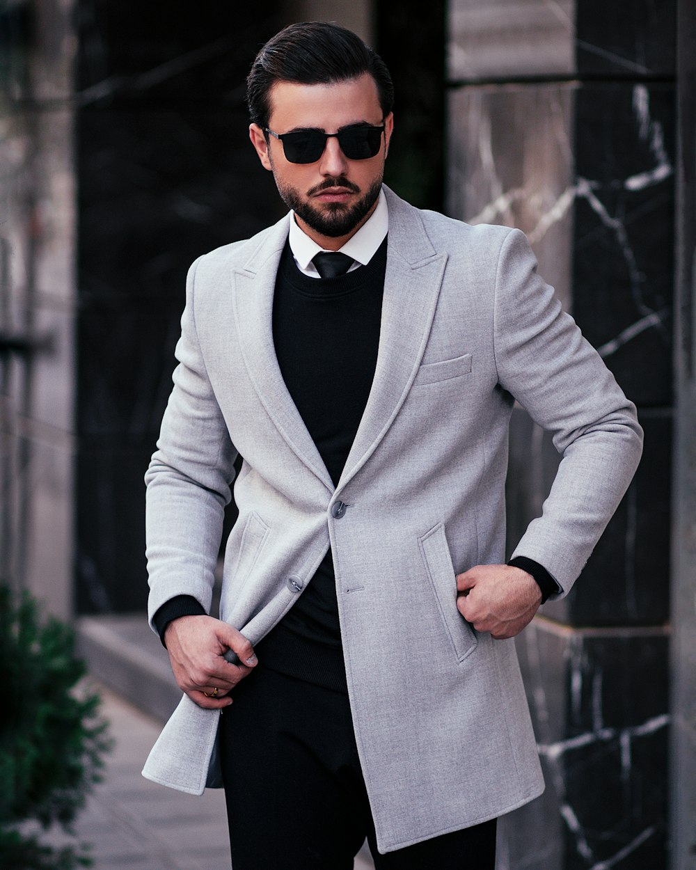 a man in a suit and sunglasses standing on a sidewalk