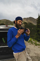 A friendly mechanic smiling outdoors with a mountain backdrop.
