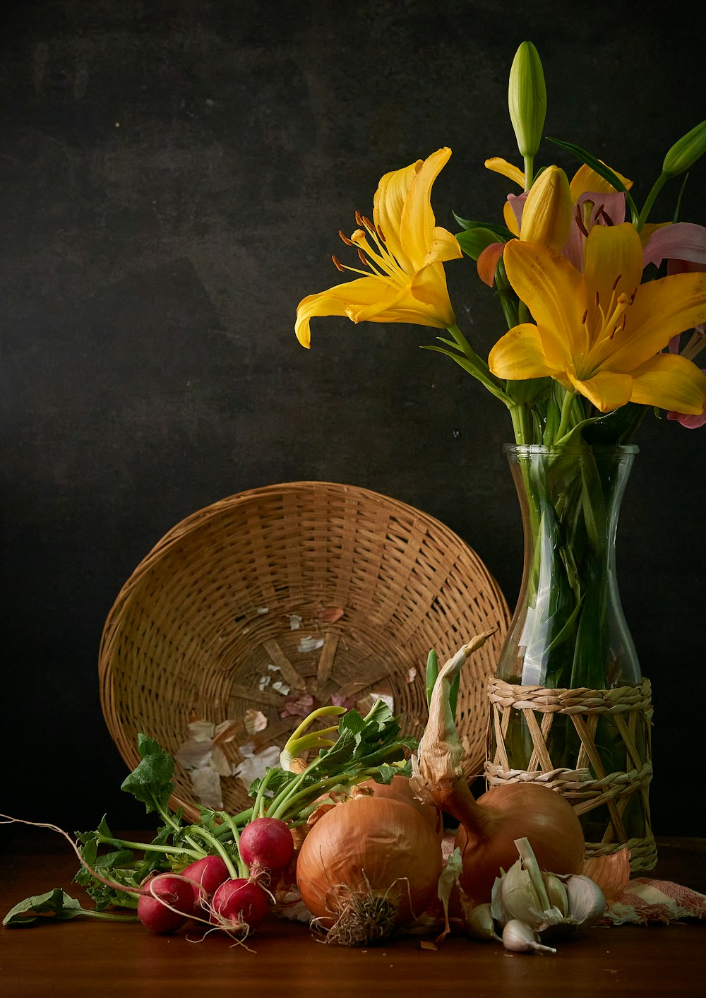 a vase filled with yellow flowers next to onions and radishes