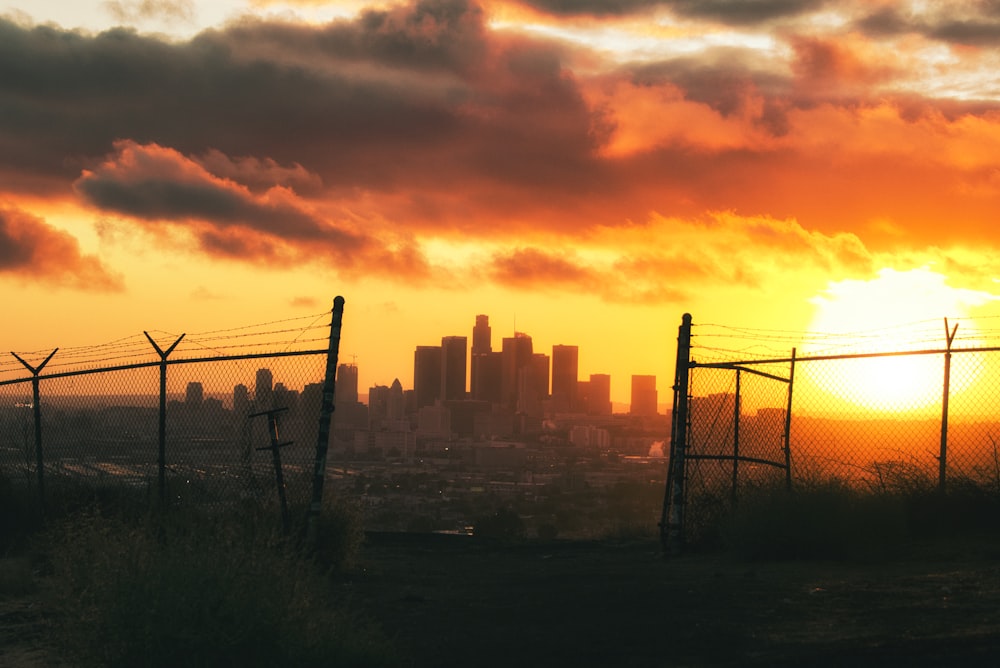 the sun is setting behind a fence with a city in the background