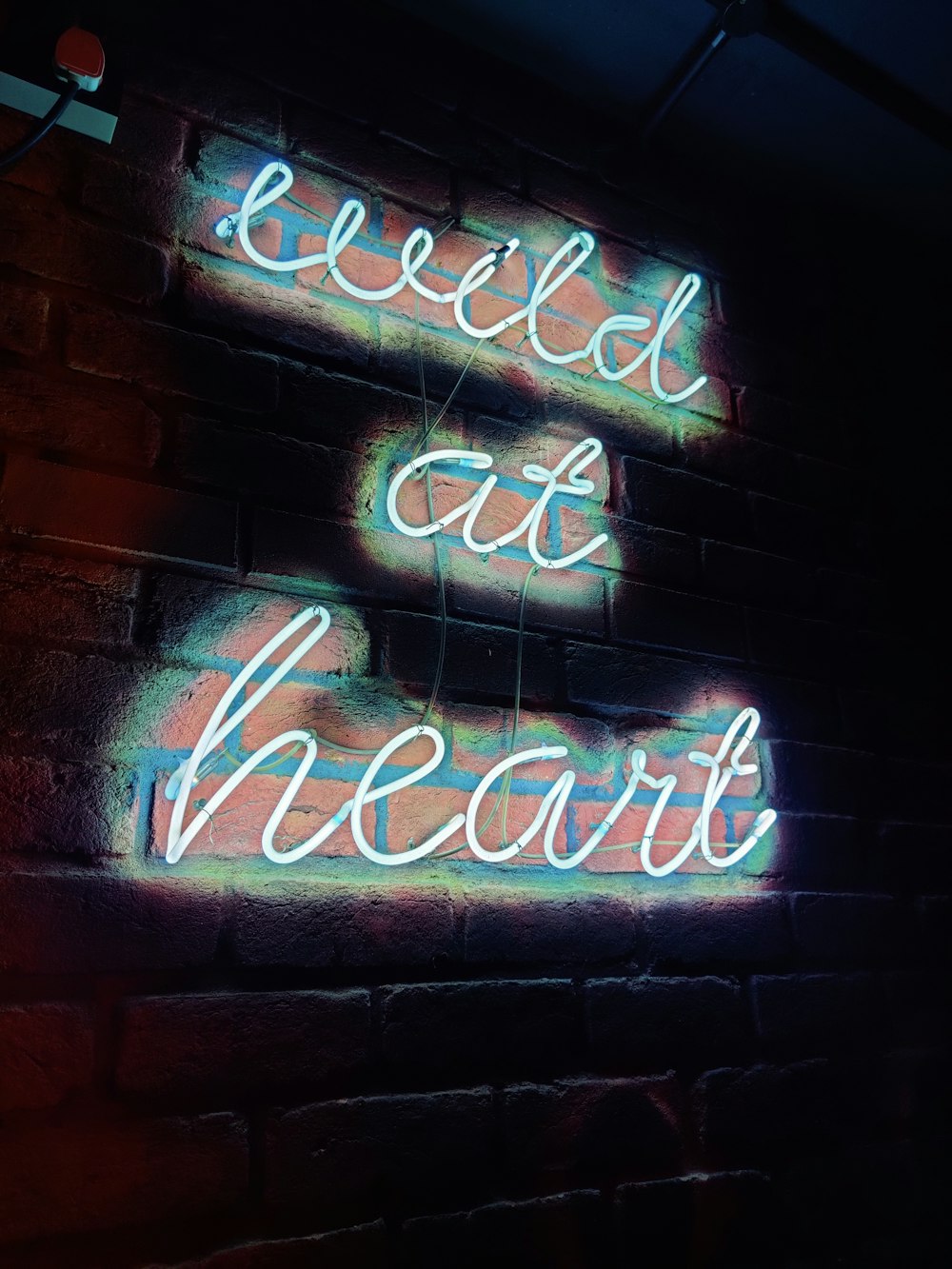 a neon sign on a brick wall that says bleed out heart