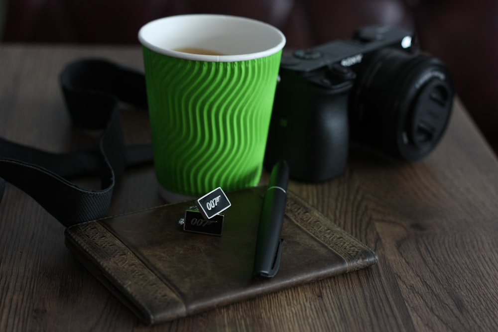 uma xícara de café sentada em cima de uma mesa ao lado de uma câmera