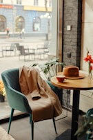 An airy coffee shop scene with a soft brown scarf casually tossed over a chair next to a journal and pen.