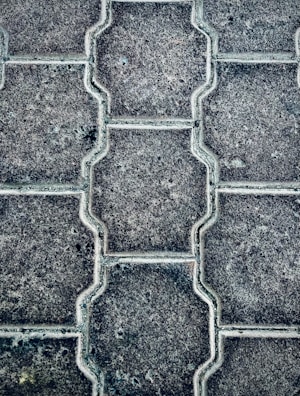 Close-up view of a textured pattern created by interlocking paving stones. The stones have a uniform shape with a consistent texture and subtle color variations.