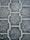 Close-up view of a textured pattern created by interlocking paving stones. The stones have a uniform shape with a consistent texture and subtle color variations.