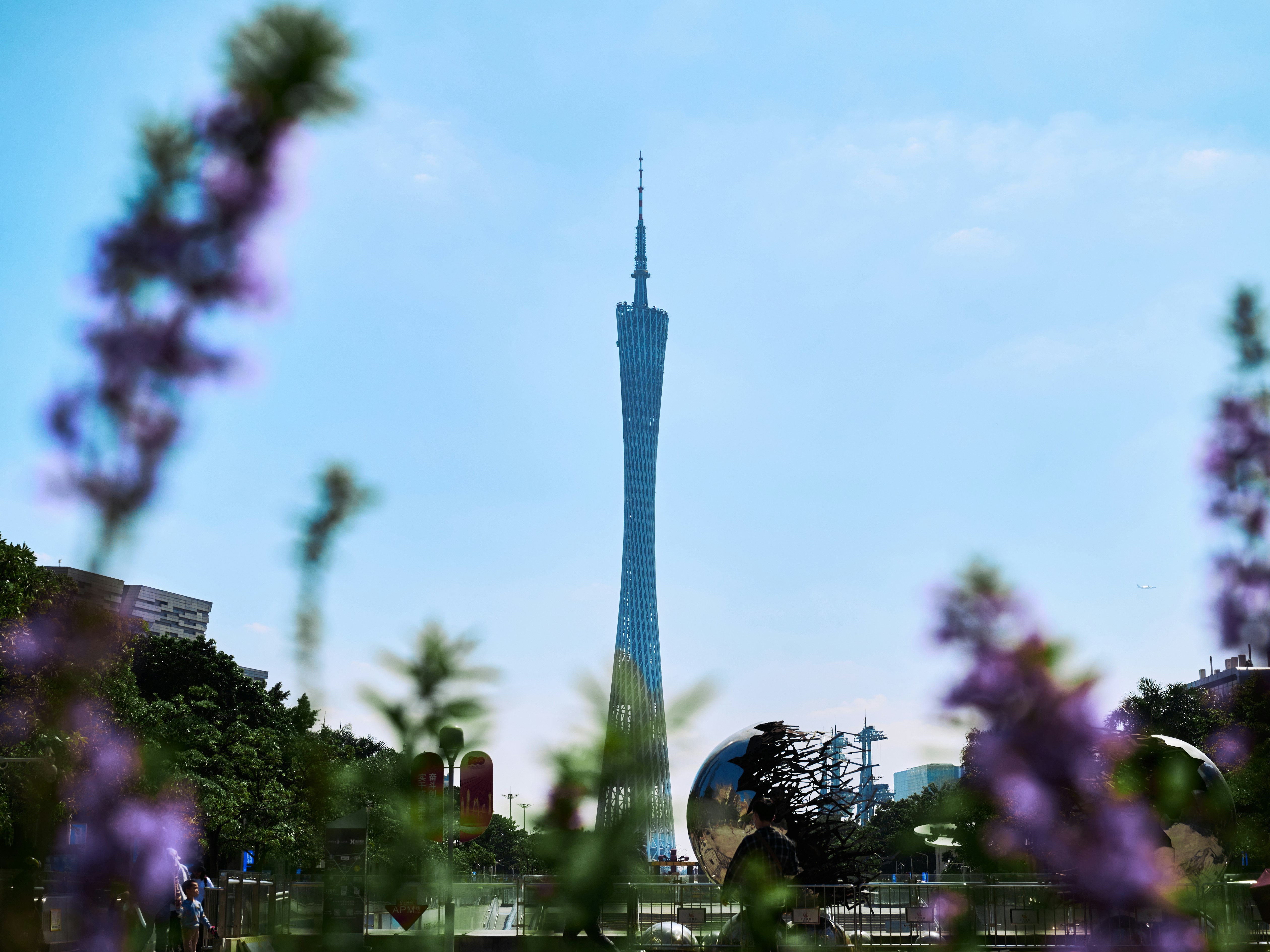 Una torre alta que se eleva sobre una ciudad junto a flores púrpuras
