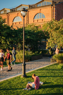 A vibrant city park with people enjoying a sunny day, walking dogs and reading books.