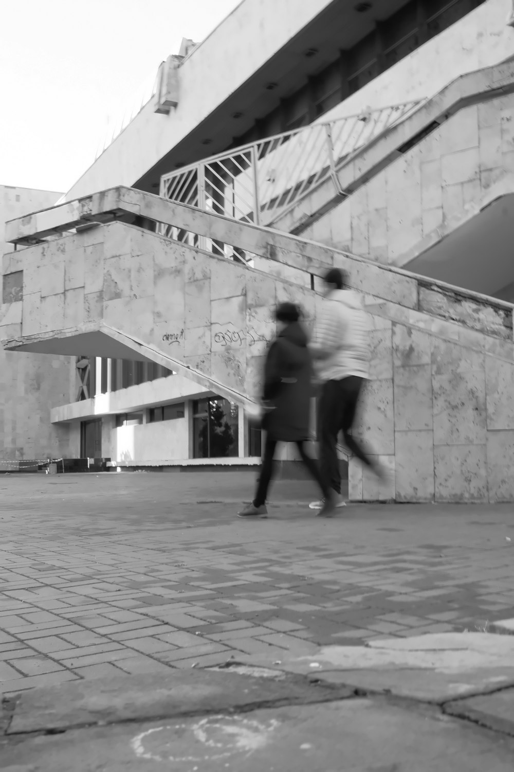 a couple of people walking down a sidewalk next to a building