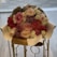 A bouquet of various colored roses and small flowers wrapped in elegant paper. The bouquet features prominently pink and red roses, with accents of white and purple flowers. It is placed on a decorative stand with a soft, blurred background.