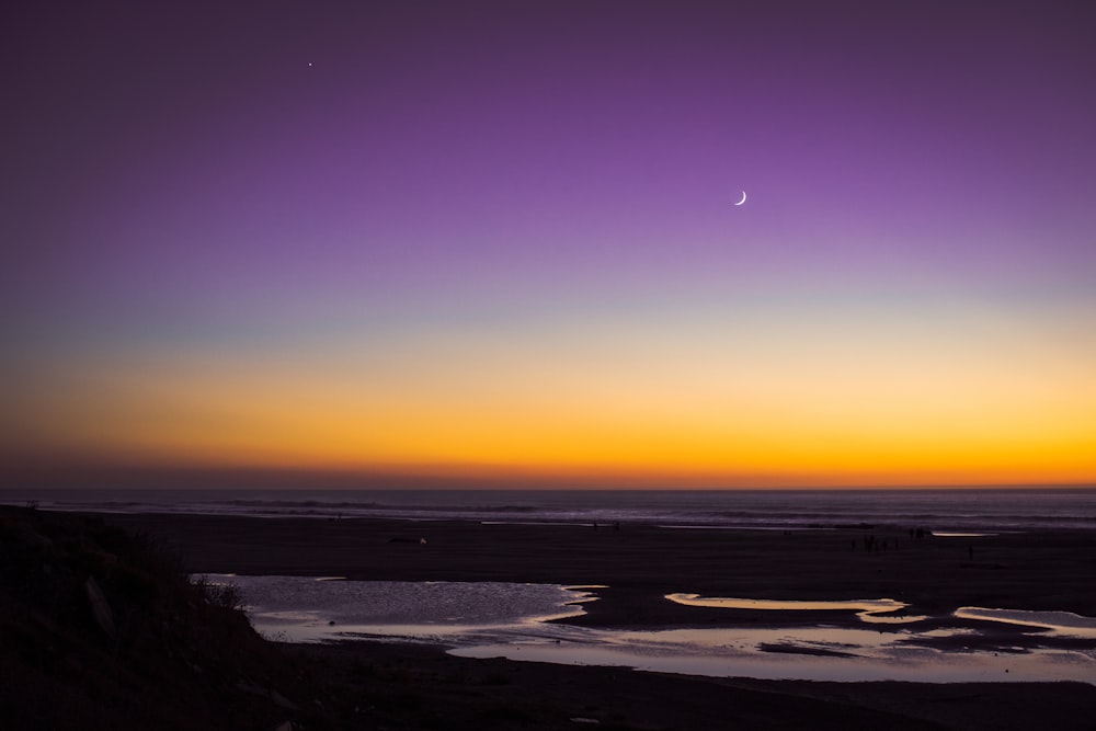 El sol se está poniendo sobre el océano con una luna en el cielo