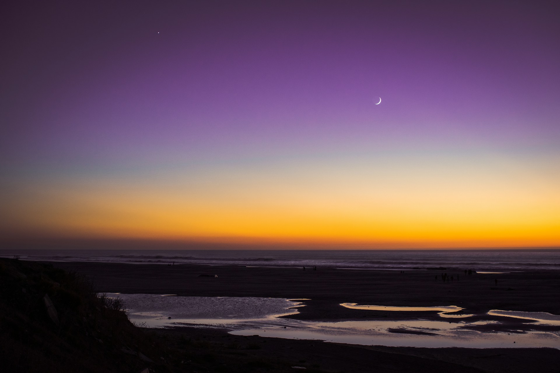 the sun is setting over the ocean with a moon in the sky